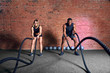 © alfa27 - Multiethnic fitness couple training cardio workout together, exercising with battle ropes at indoor gym.