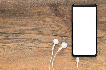 Smartphone with isolated white screen with connected earphones on the background of a wooden desk