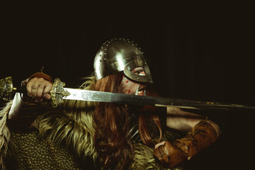 Viking warrior with metallic helmet and animal skins. leather gauntlets, red wooden shield with gold decorations and steel sword