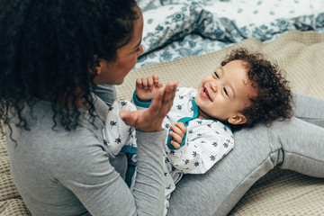 Wall Mural - Happy child lying on mother hips. Mother playing with son.