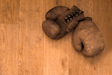 Boxing Gloves. Old Vintage Retro Pair Of Leather Worn Mittens Are On The Wood Table. Red Colors And Soft Lights. Gloves Of Retired Boxer And Fighter