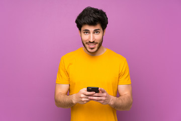 Handsome over isolated purple wall sending a message with the mobile