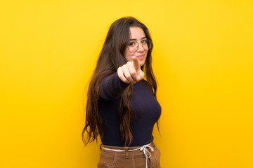 Teenager girl over isolated yellow wall points finger at you with a confident expression