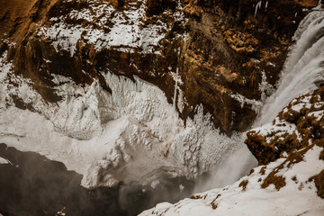 beautiful view of a waterfall and birds flying around the mountains in Iceland with snow covering rocks 