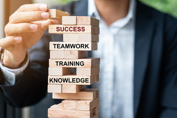 Businessman hand placing or pulling wooden block on the tower with text; Success, Teamwork, Training and Knowledge. Business concepts