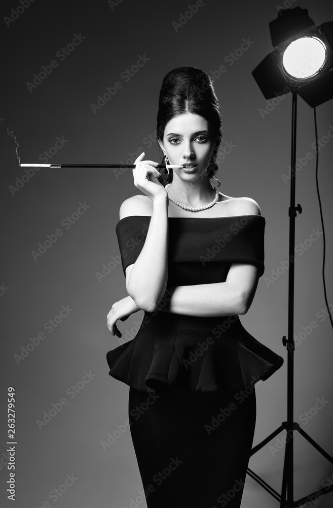 Retro shot: beautiful young woman smoking cigarette. Vintage portrait of  posh girl in 60s style. Seductive lady in black dress and pearl necklace.  Black and white Stock-bilde