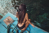 Fototapeta Na drzwi - A young sexy filipino girl sitting on a fishing boat with her black swimsuit enjoying the ocean breeze in the Philippines