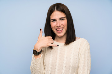 Young woman over isolated blue wall making phone gesture