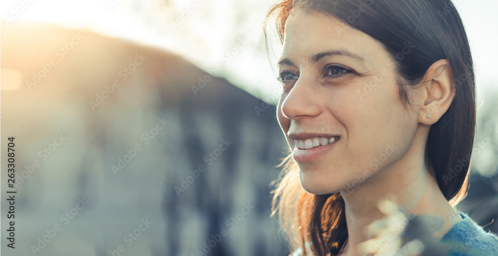 Closeup of a smiling young woman looking into the distance at sunset. - obrazy, fototapety, plakaty 