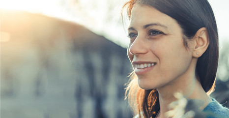 Closeup of a smiling young woman looking into the distance at sunset.