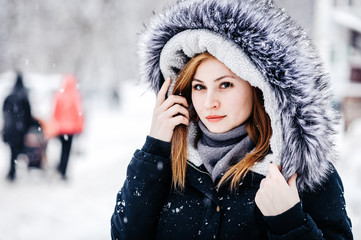 Outdoor portrait of young beautiful girl wearing in black jacket with a hood . Model posing in street. Winter holidays concept.