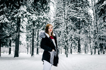 Wall Mural - Portrait of a girl in the black jacket with fur hood amid winter forest