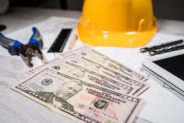 Construction industry costs money us dollars banknotes by tools safety equipment and blueprints