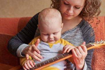 Wall Mural - Mom teaches her little son to play the guitar. Early child development.