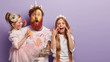 canvas print picture - Horizontal shot of shocked dad has yellow face painted with watercolors, two children have fun with father, joyful expressions, isolated over purple background with free space for promotion.