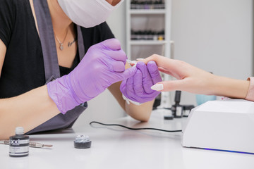 Wall Mural - Manicurist work on a woman client hands, make her nails look beautiful. Salon procedure in process. Professional works in gloves for sterility