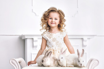 Little beautiful and cute girl in a fashionable festive dress with animals rabbits in a white interior