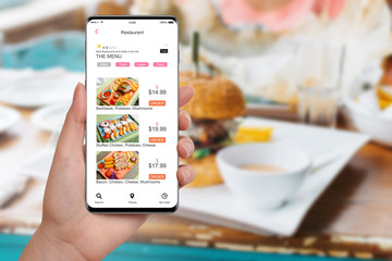 Girl in restaurant ordering food on her smartphone, blurred table with food in background