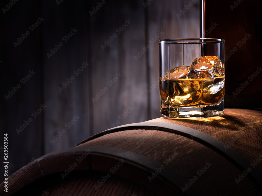 Glass of whiskey with ice cubes on the wooden barrel with wooden background - obrazy, fototapety, plakaty 