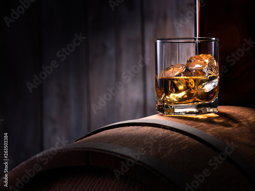 Fotografía Glass of whiskey with ice cubes on the wooden barrel with wooden background