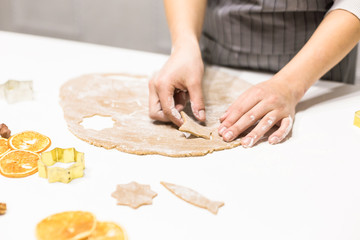 Wall Mural - Young pretty woman prepares the dough and bakes gingerbread and cookies in the kitchen. She makes a star shape on the dough. Merry Christmas and Happy New Year.