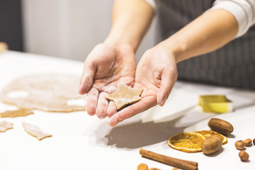 Wall Mural - Young pretty woman prepares the dough and bakes gingerbread and cookies in the kitchen. She holds a star cut from the dough in her hands. Merry Christmas and Happy New Year.