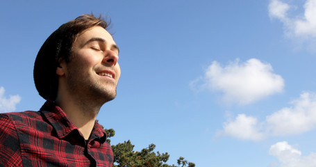 Portrait of an authentic and genuine hipster man smiling on a blue sky with white clouds background.