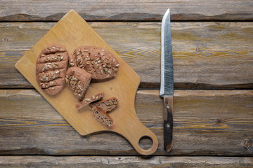 whole wheat bread with sunflower seeds and knife with cutting board and burlap on wooden background, top view 