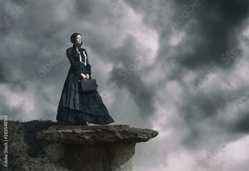 Fototapeta Outdoors portrait of a victorian lady in black standing on the cliff.