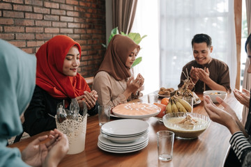 Wall Mural - asian muslim people praying before having their food in dining room together for break fasting