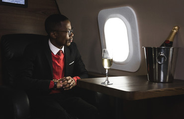 Successful young Afro American black businessman sitting in the chair of his private jet