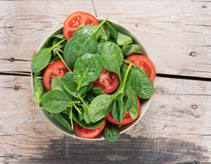 Wall Mural - spinach and tomato salad on a wooden table. top view