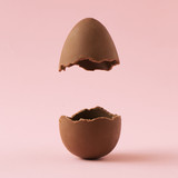 Fototapeta Kwiaty - Chocolate Easter egg broken in half on pastel pink background with creative copy space. Minimal Easter holiday concept.