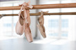 Old pointe shoes hang on ballet wooden barre in dance class room. Light sunny blurred background of ballet classic school. Reflection in mirror.