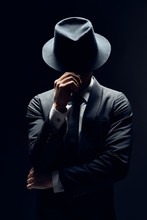 Man In Suit Hiding Face Behind His Hat Isolated On Dark Background