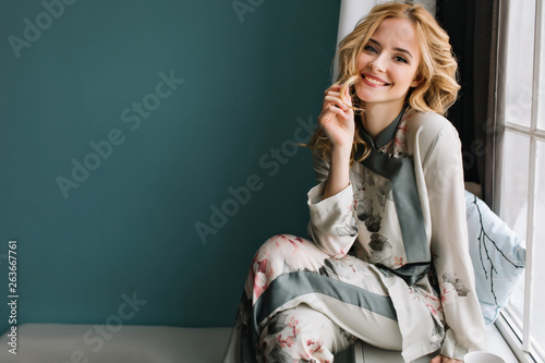 Beautiful Young Woman With Long Blonde Wavy Hair Sitting On Window