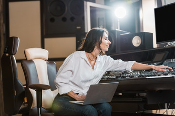 Wall Mural - attractive, smiling sound producer using laptop and working at mixing console in recording studio