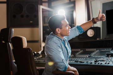 Wall Mural - smiling mixed race sound producer showing thumb up while working in recording studio