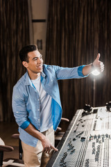 Canvas Print - cheerful mixed race sound producer showing thumb up while working at mixing console