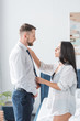 © LIGHTFIELD STUDIOS - attractive woman touching shirt of handsome bearded man standing in formal wear