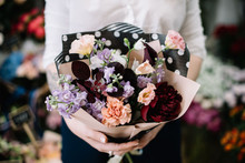 Very Nice Young Woman Holding Beautiful Blossoming Flower Bouquet Of Fresh Carnations, Peony, Manitoba In Pink, Lavender And Burgundy Colors On The Flower Stalls Background At The Florist Shop