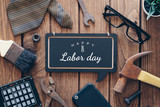 Fototapeta  - Happy Labor day background concept. Flat lay of construction blue collar handy tools and white collar's accessories over wooden background with text Happy Labor day on black chalkboard.