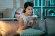 © PR Image Factory - Chilling gorgeous asian woman on grey sofa couch at home doing online shopping on digital pad. female relax in comfortable house dark design interior indoors at night. young elegant lady using tablet