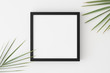 © Snoflinga - Top view of a black square frame mockup with palm leaf decoration.