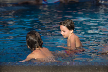 Wall Mural - Adorable happy little child, toddler boy, having fun relaxing and playing in a pool on sunny day during summer vacation