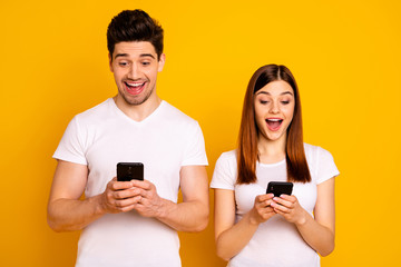 Portrait of his he her she two nice attractive charming stylish trendy cheerful cheery people using new cool chatting gadget device isolated over vivid shine bright yellow background