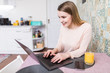 © F8  \ Suport Ukraine - Smiling young woman using laptop in the kitchen at home