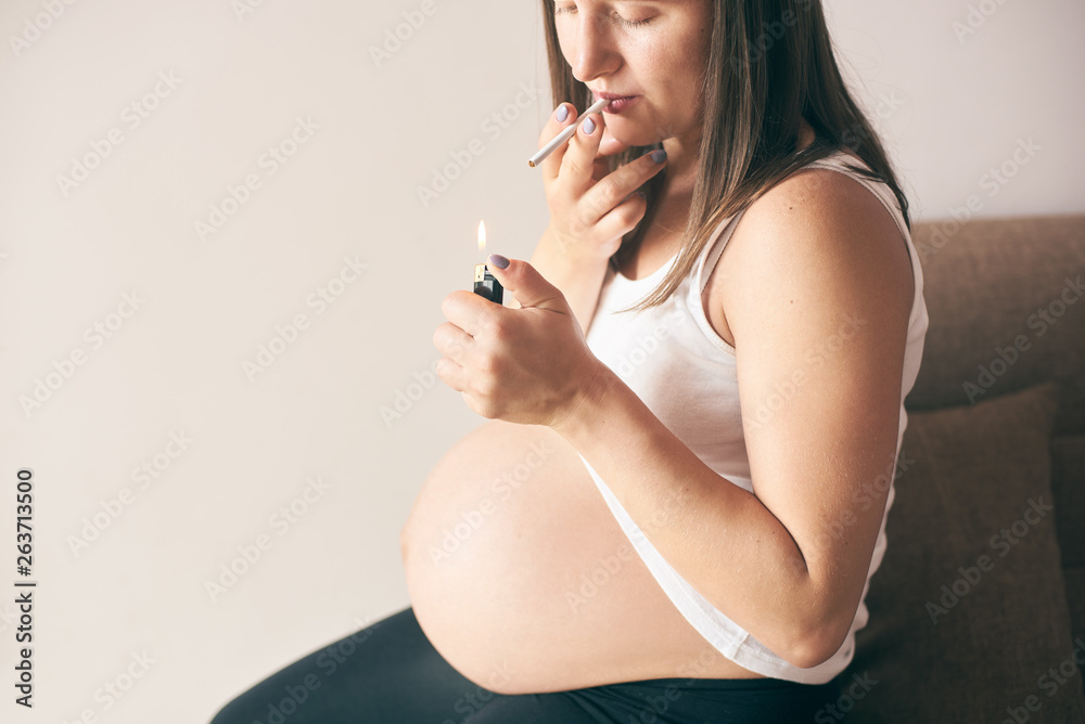 cigarette smoking during pregnancy Close up view of lighter and cigarette in hands of pregnant woman. Young  future mother in white shirt smoking during pregnancy period. Concept of  threat and harmfulness. Stock Photo