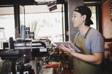 asian man barista holding tablet for checking order from customer on coffee cafe.