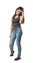 Young Woman In Sleeveless Gray Top And Blue Jeans Standing And Looking Down With Hand Raised To Forehead Isolated On White Background.